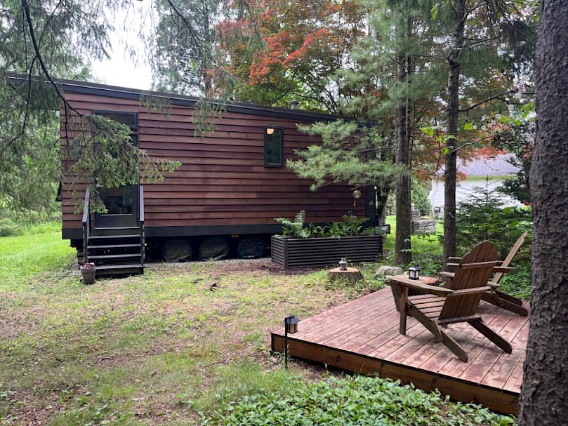 Beautiful modern cedar-clad tiny house on wheels with raised greywater mulch basin nestled in the woods.